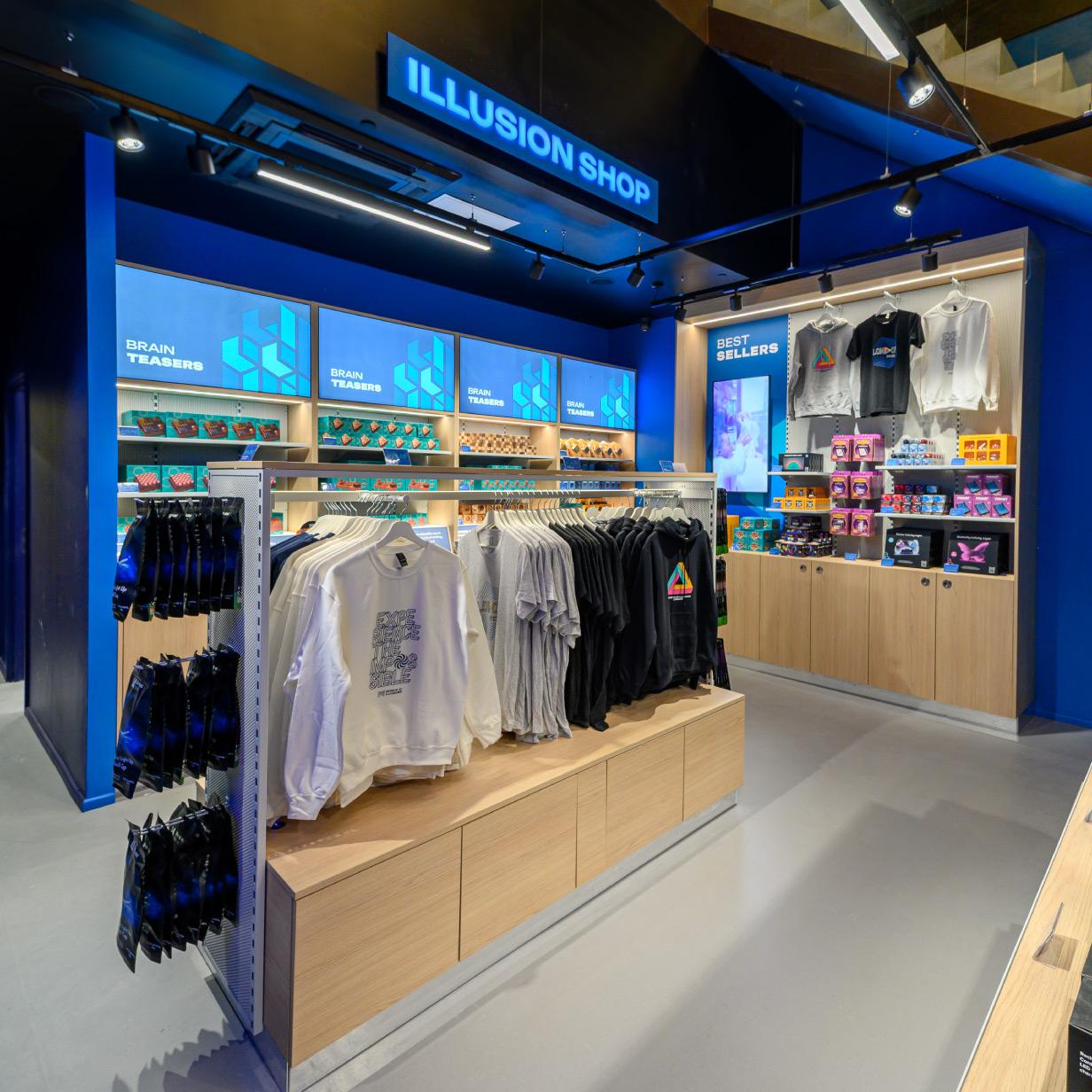 Interior of Museum of Illusions shop with shelves of branded merchandise, apparel, and interactive illusion items displayed in a modern retail space.