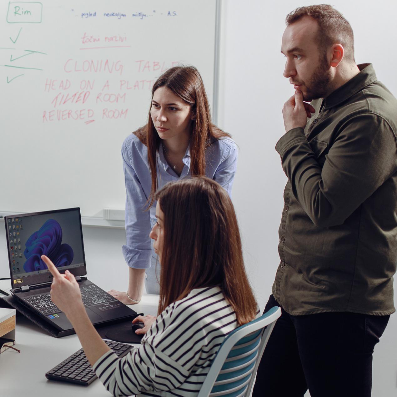 Team members collaborating around a workstation, reviewing ideas and discussing work in a modern office environment.