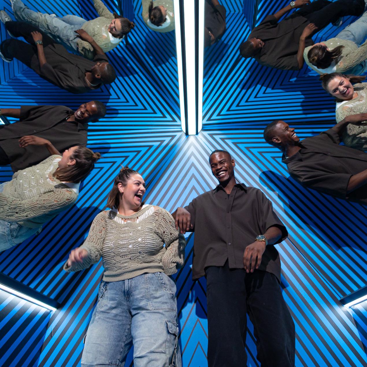 Visitors experiencing a mirrored illusion room with infinite reflections and blue optical design at the Museum of Illusions.