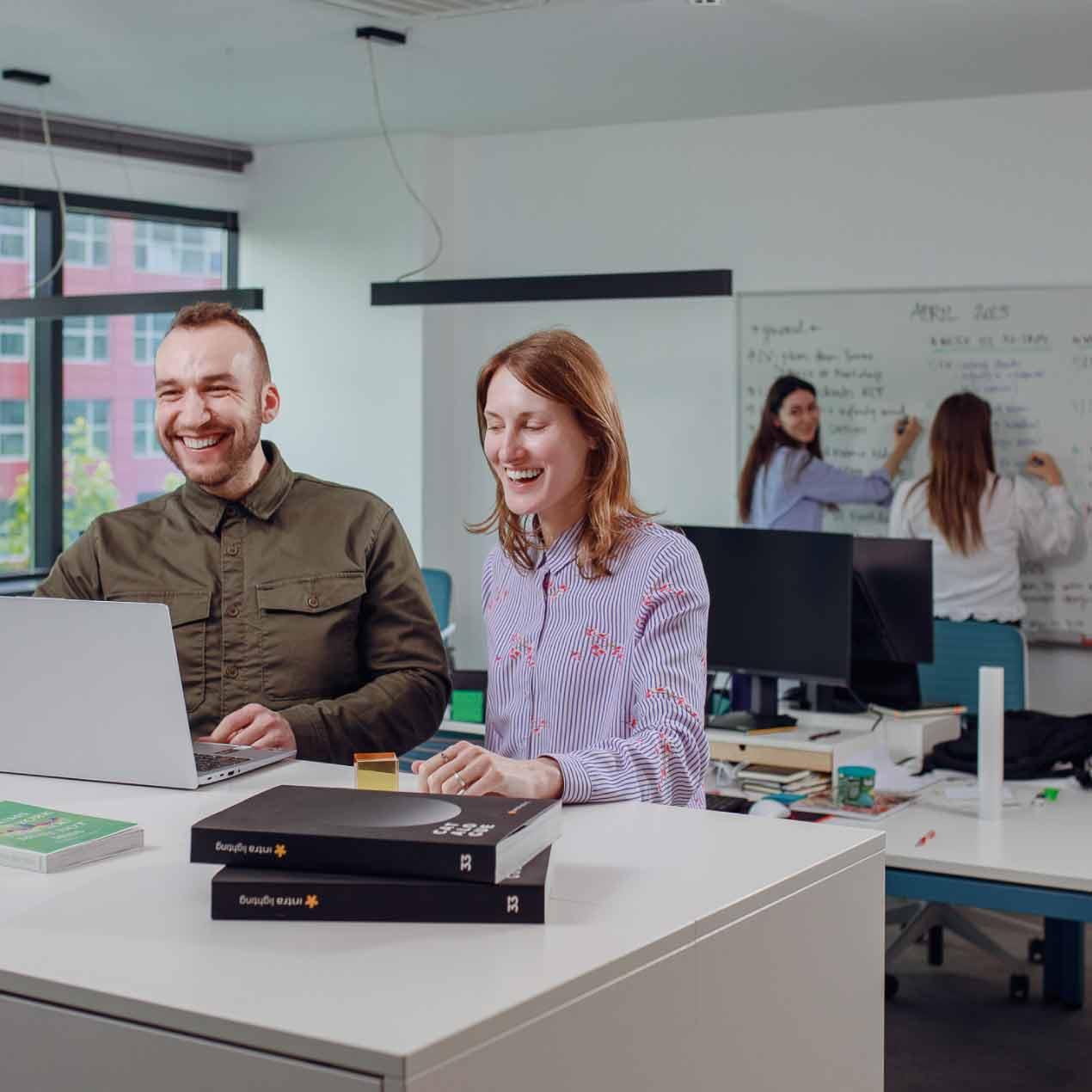 Team members collaborating around a workstation, reviewing ideas and discussing work in a modern office environment.