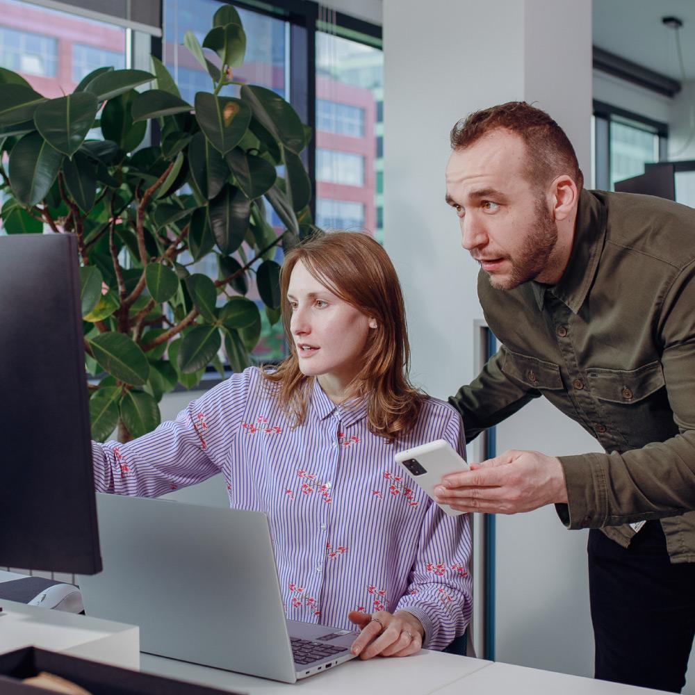 Team members working together at a desk, reviewing content on a computer screen and coordinating tasks