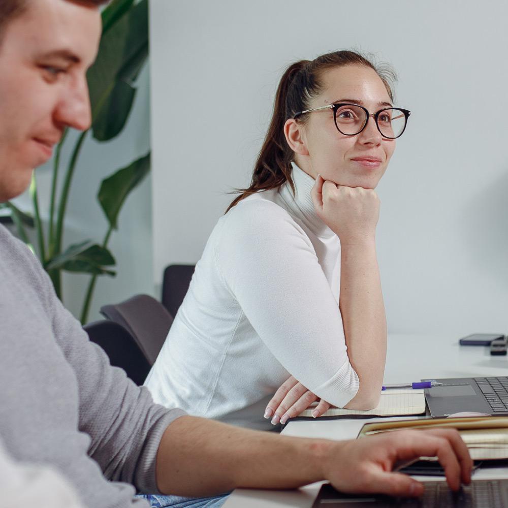Person seated at a desk looking toward colleagues while reviewing notes during a collaborative work session.